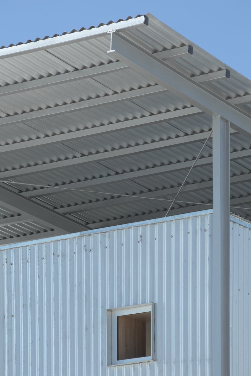 Small framed window punched into the corrugated metal wall beneath the exposed steel roof structure