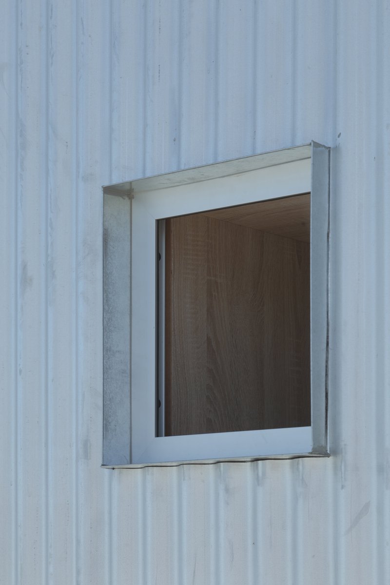 Close-up of a metal-framed window with timber infill set into vertical corrugated cladding