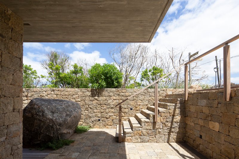 Outdoor courtyard with stone walls, a large boulder, and timber staircase under a concrete soffit