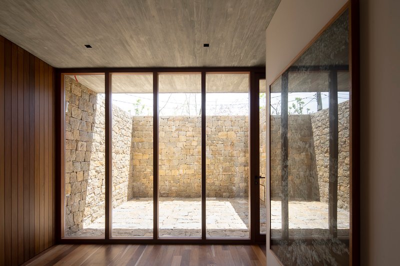 Interior view through floor-to-ceiling glazing framing the stone-walled courtyard in afternoon light