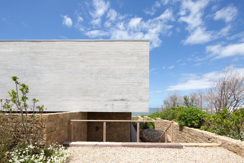 Concrete upper volume cantilevered above a recessed stone base with distant ocean views