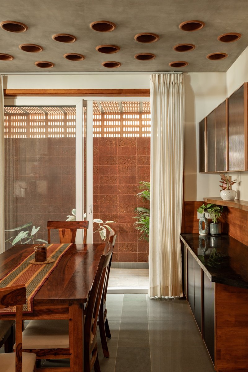 Dining area with perforated concrete ceiling opening to courtyard with terracotta tile wall and plants