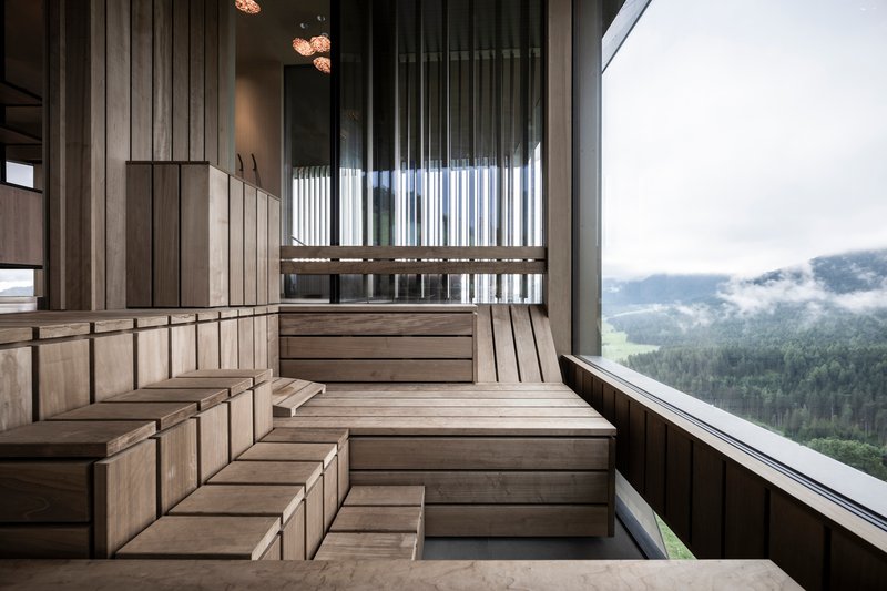 Timber sauna interior with tiered benches overlooking misty forested valley through glass wall