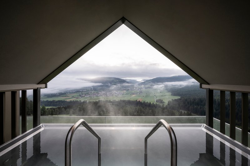 Indoor pool with house-shaped handrails framing view of misty valley and village below