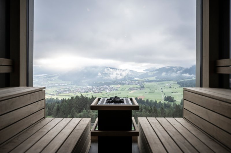 Sauna bench with heater and towel facing wide window overlooking patchwork fields and low clouds