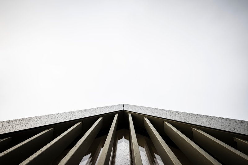 Upward view of vertical concrete fins meeting aggregate coping under pale sky