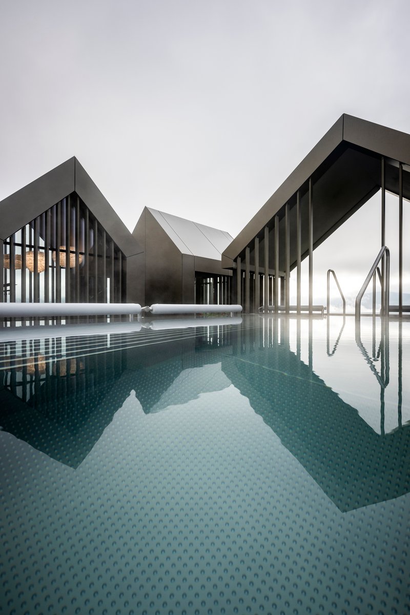 Rooftop pool with dark tile surface reflecting the angular gabled volumes under an overcast sky