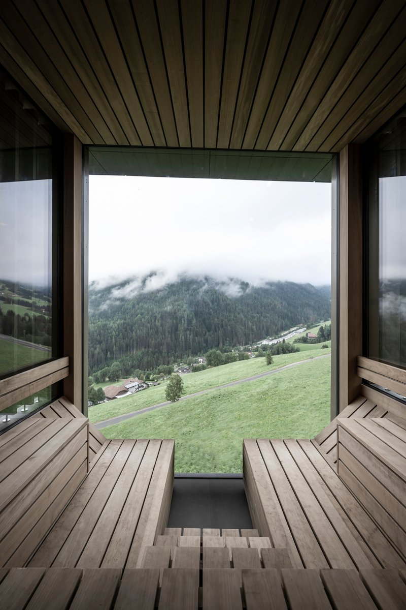 Timber sauna interior with slatted benches facing a picture window overlooking green meadows and mist