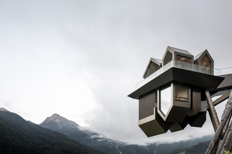 Cantilevered viewing platform with faceted metal panels set against fog-shrouded mountain peaks