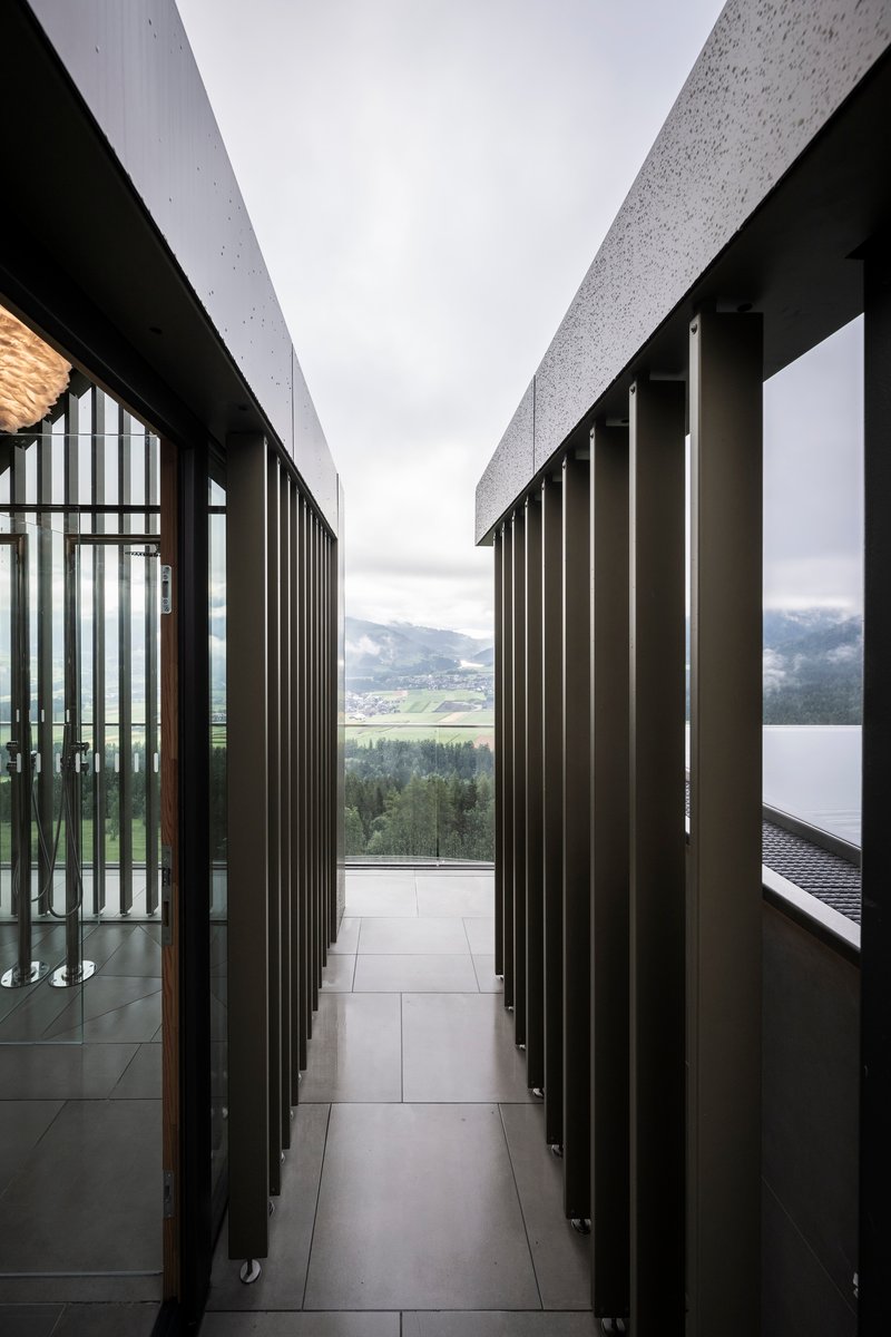 Narrow corridor with vertical metal screening opening to a lakeside mountain vista