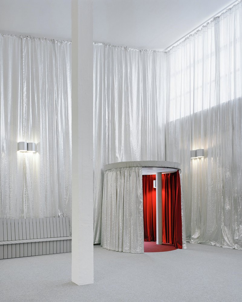 Foyer with floor-to-ceiling silver curtains surrounding a cylindrical entrance draped with red velvet inside
