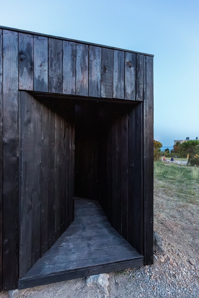 Recessed entrance through blackened timber walls leading to a dark interior corridor at dusk