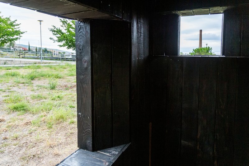Interior threshold space with charred timber walls framing horizontal window openings to the landscape