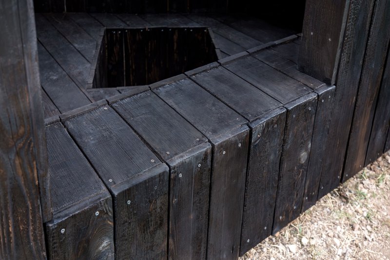 Detail of blackened timber planks forming a bench edge beside the floor opening