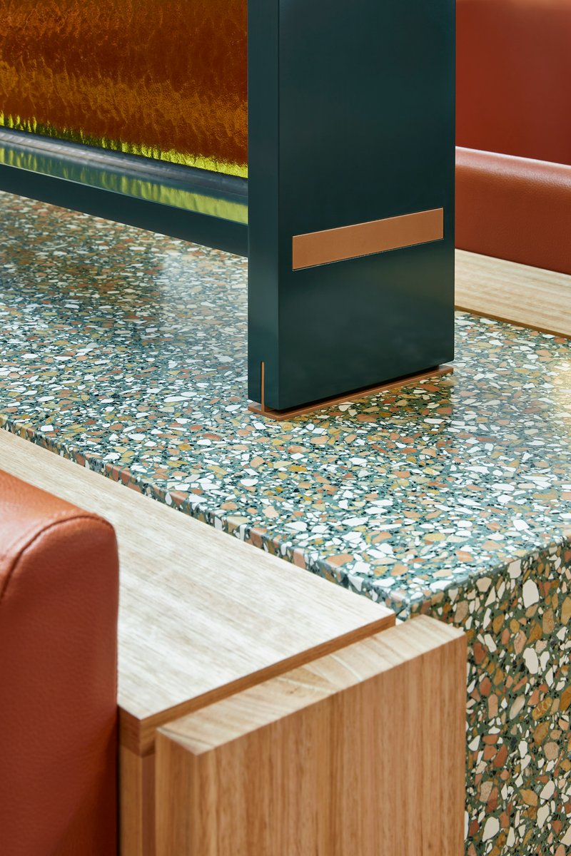 Detail of terrazzo countertop meeting dark painted column with bronze metal accent strip