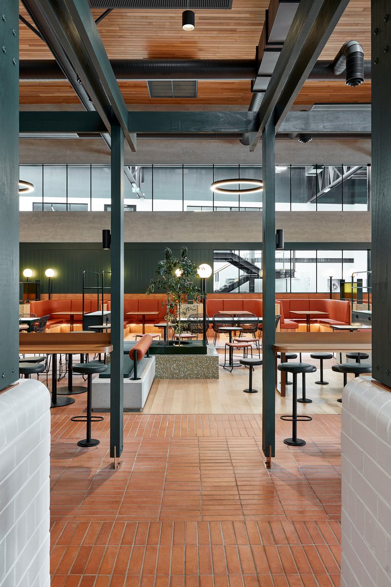 View through the double-height interior showing steel structure, timber ceiling slats, and seated dining areas