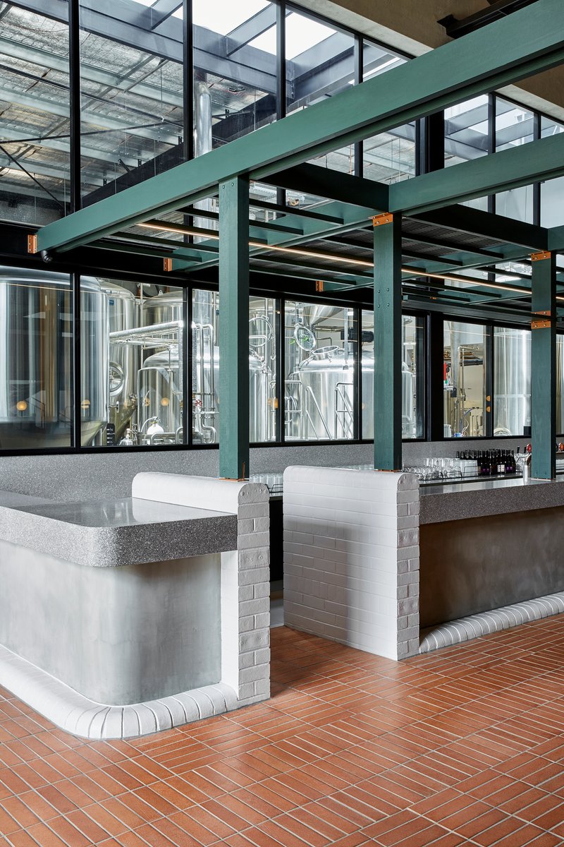 Banquette seating with terrazzo counters and white tiled bases beneath steel mezzanine structure