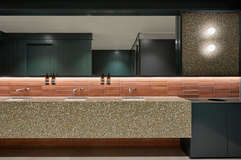 Bathroom vanity with terrazzo countertop and terracotta tile backsplash beneath dark green cabinetry