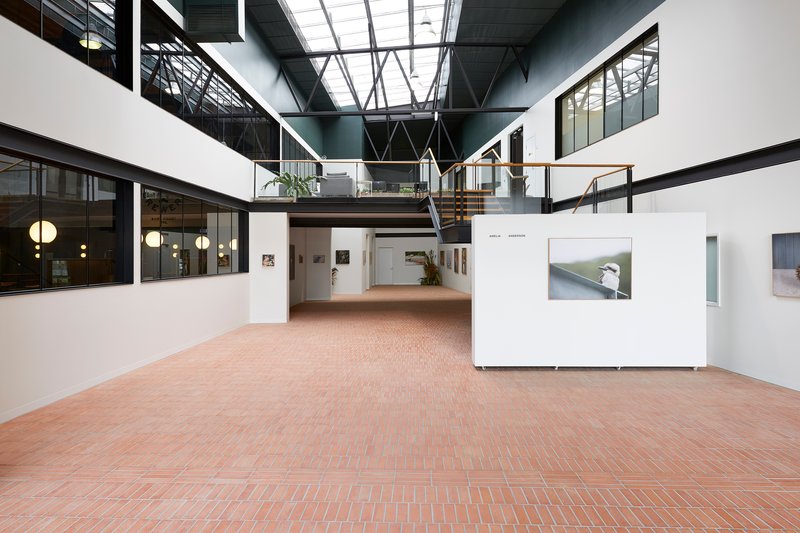 Double-height atrium with mezzanine walkway, skylights and freestanding white exhibition panels on herringbone brick floor