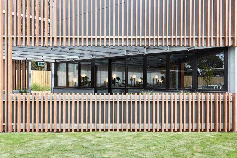 Exterior facade with vertical timber screen wrapping glass windows above a manicured lawn