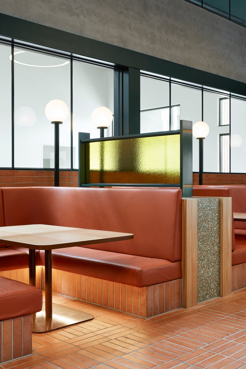 Booth seating with terracotta tile base and teal upholstery below a backlit brass panel and globe fixtures