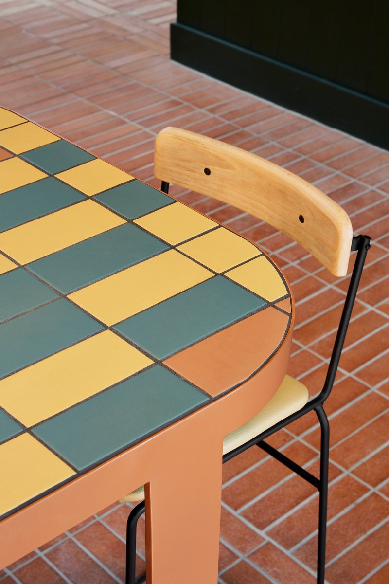 Tabletop with yellow and grey checkered tiles beside a wooden chair on herringbone brick flooring