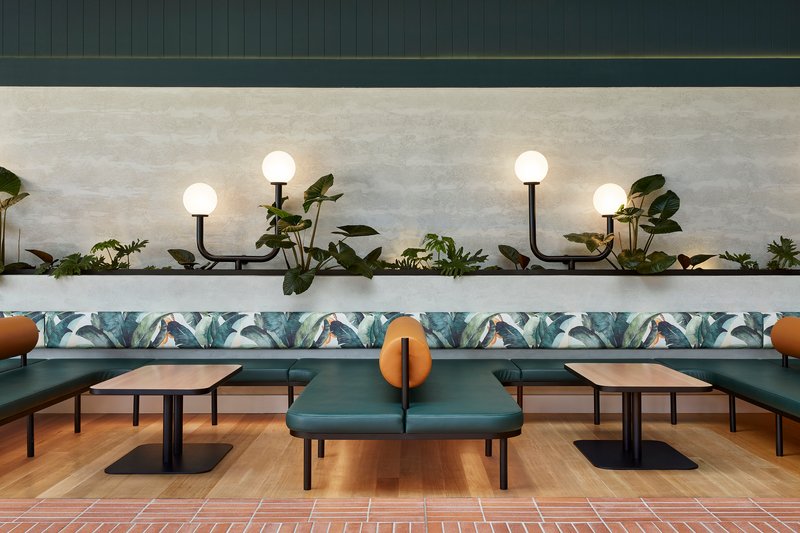 Symmetrical view of booth seating with botanical upholstery and planted ledge illuminated by globe sconces