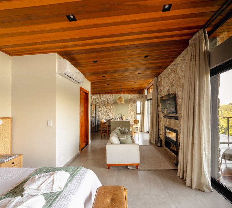 Open-plan bedroom and living space with timber-slatted ceiling and stone accent wall enclosing a fireplace