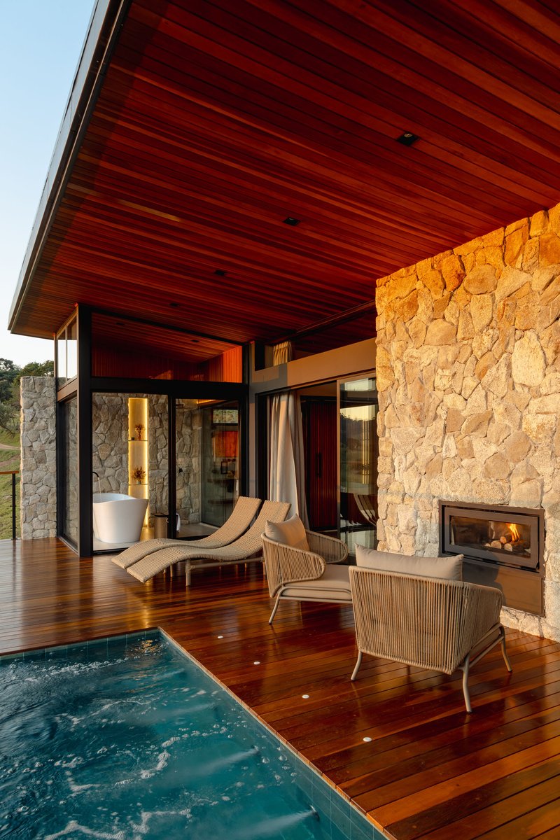 Covered terrace with timber deck, plunge pool, stone fireplace wall, and linear timber ceiling in afternoon light