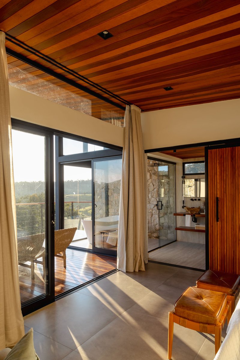 Bedroom interior looking through glazed doors to timber deck with stone walls and timber ceiling above