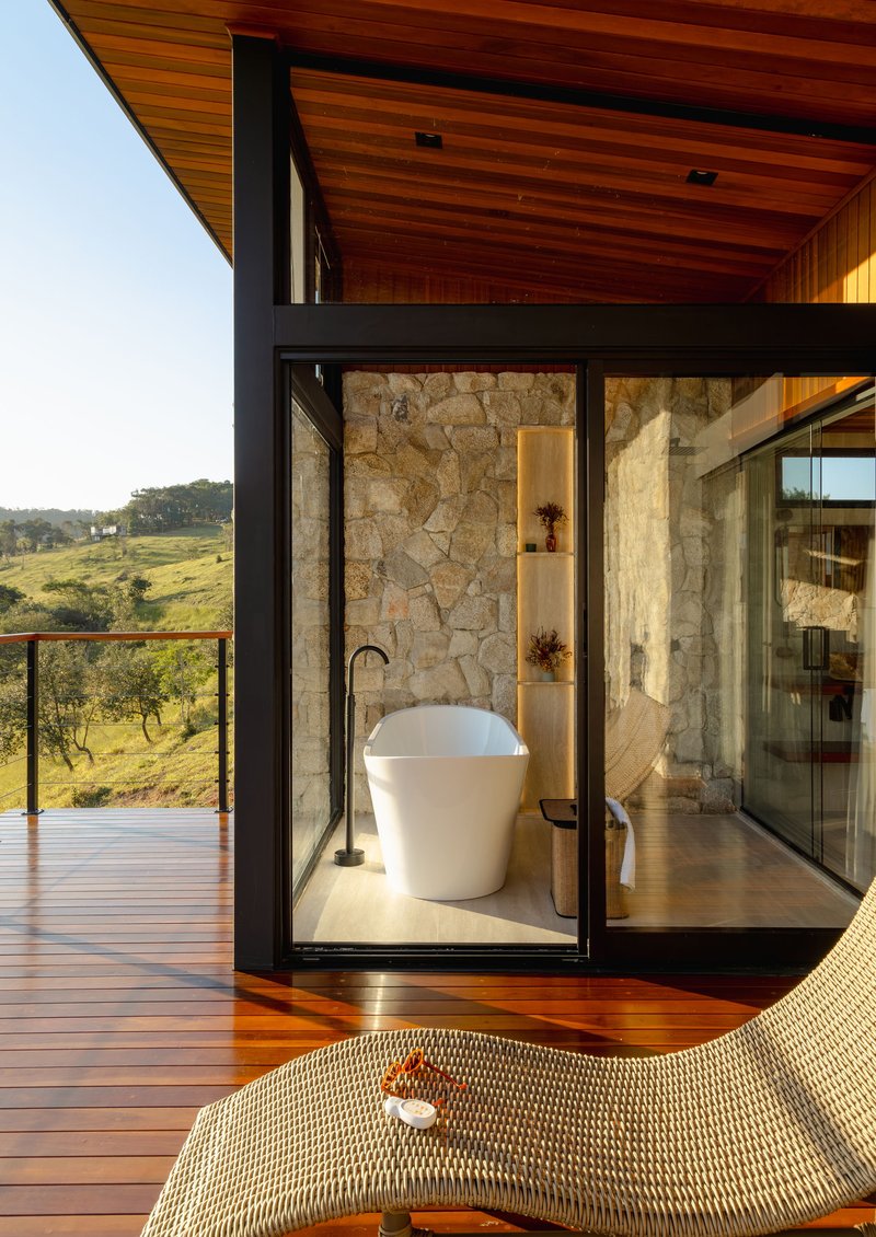 Glass-enclosed bathtub alcove with stone walls opening to timber deck and valley views at sunset