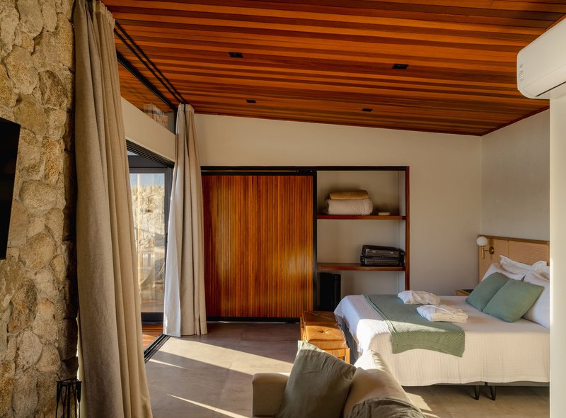 Bedroom with timber slat ceiling and stone column beside floor-to-ceiling curtains in afternoon sunlight