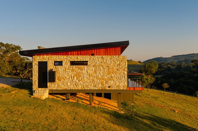 Hillside elevation showing rough stone walls and corrugated metal base beneath a dark cantilevered roof