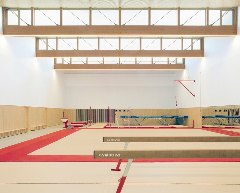 Gymnastics hall with tiered timber clerestory monitors above beams and maroon floor mats