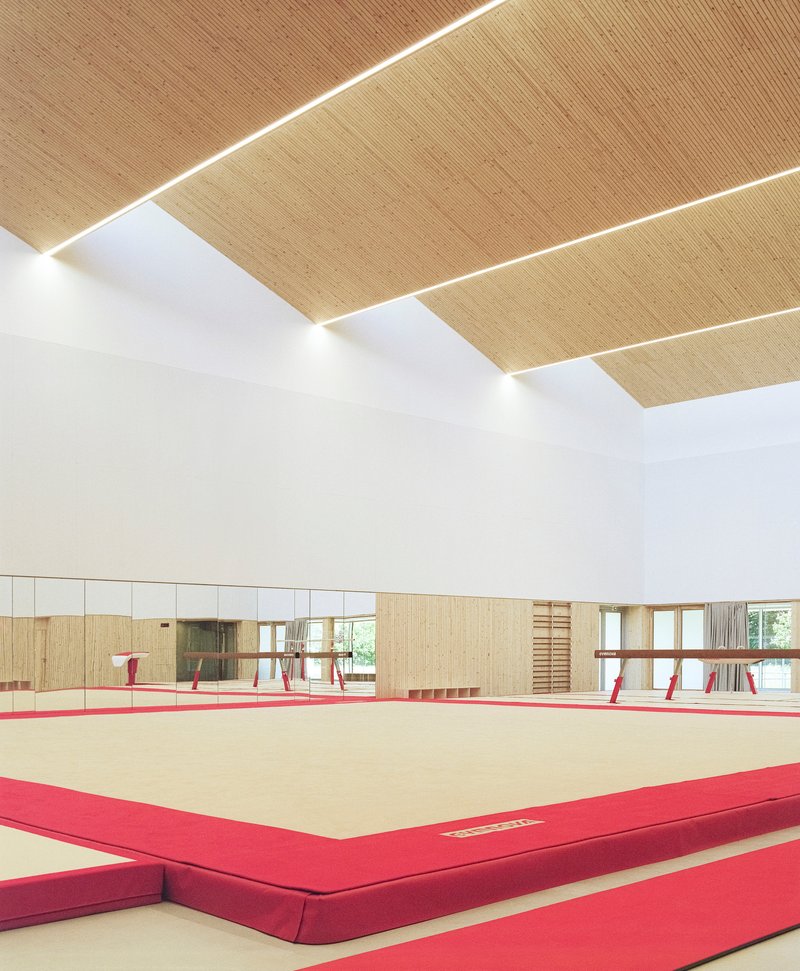 Interior view showing woven ceiling panels with linear lighting slots above the gymnastics floor