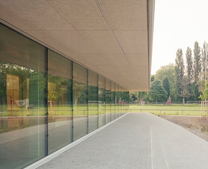 Covered walkway with continuous glazing reflecting sports field and trees beyond under fibrous ceiling panels