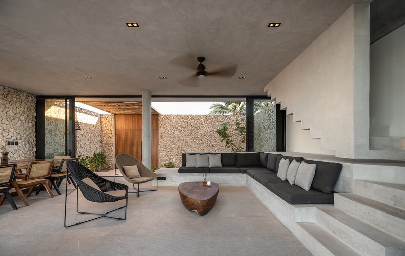 Sunken living room with built-in concrete seating opening to a courtyard with stone walls and palms