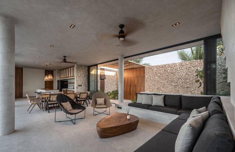 Open-plan living space with concrete ceiling and large opening framing a courtyard with stone wall