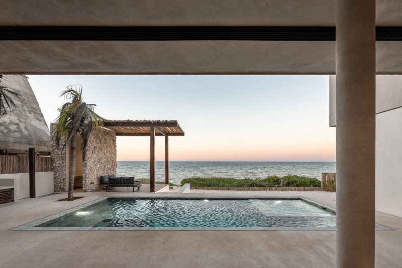 Pool terrace framed by concrete beams with ocean view and thatched pavilion at dusk