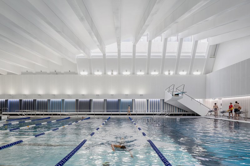 Indoor lap pool with diving platform under white beam ceiling and vertical ribbed wall panels