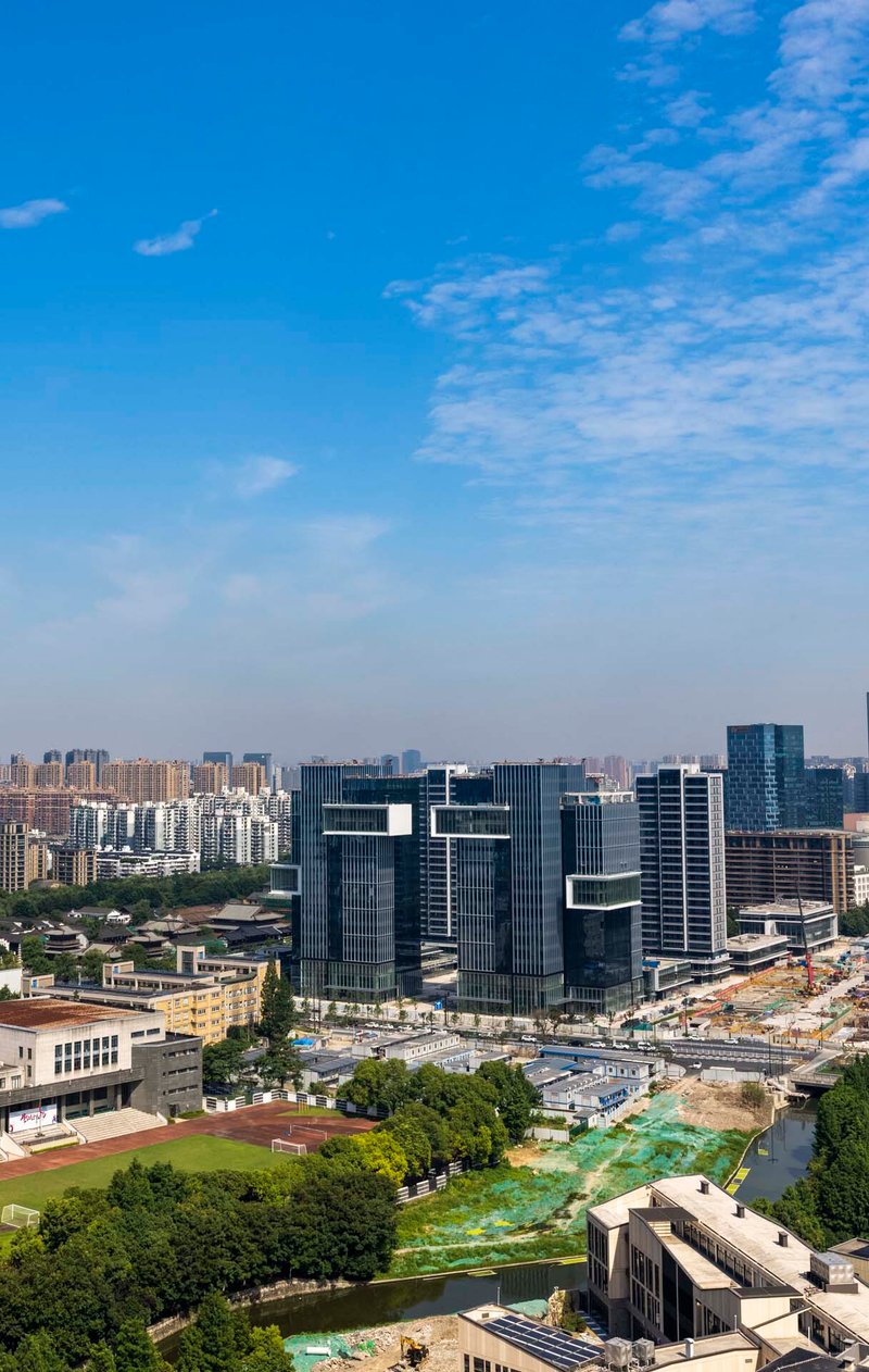 Aerial view of offset glass office towers amid low-rise buildings and a green canal corridor