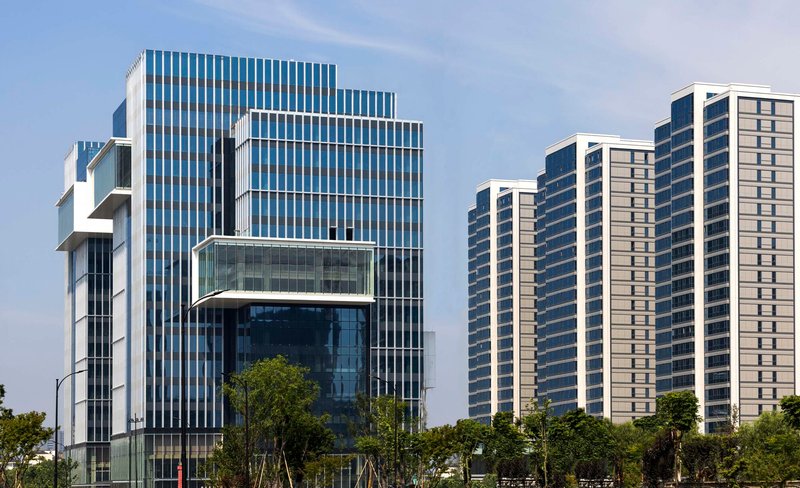 Vertical louvered glass facade with cantilevered volumes beside rows of residential high-rises