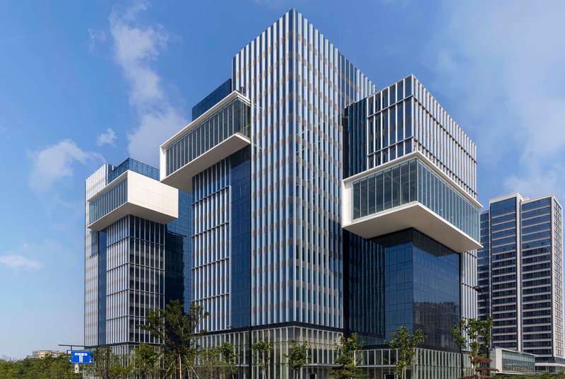 Central tower with vertical ribbed cladding flanked by cantilevered glass volumes under blue sky