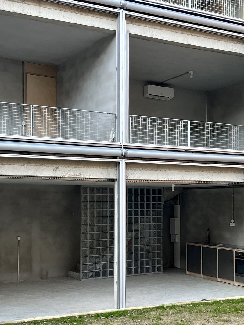 Stacked balconies with glass block walls, metal railings, and concrete soffit under overcast sky