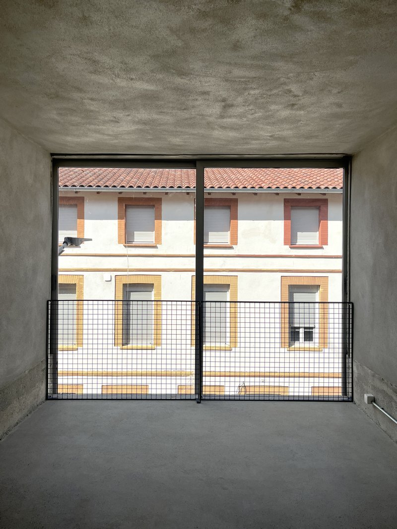 Interior room with concrete walls and floor-to-ceiling glazed doors framing view of neighboring residential facade