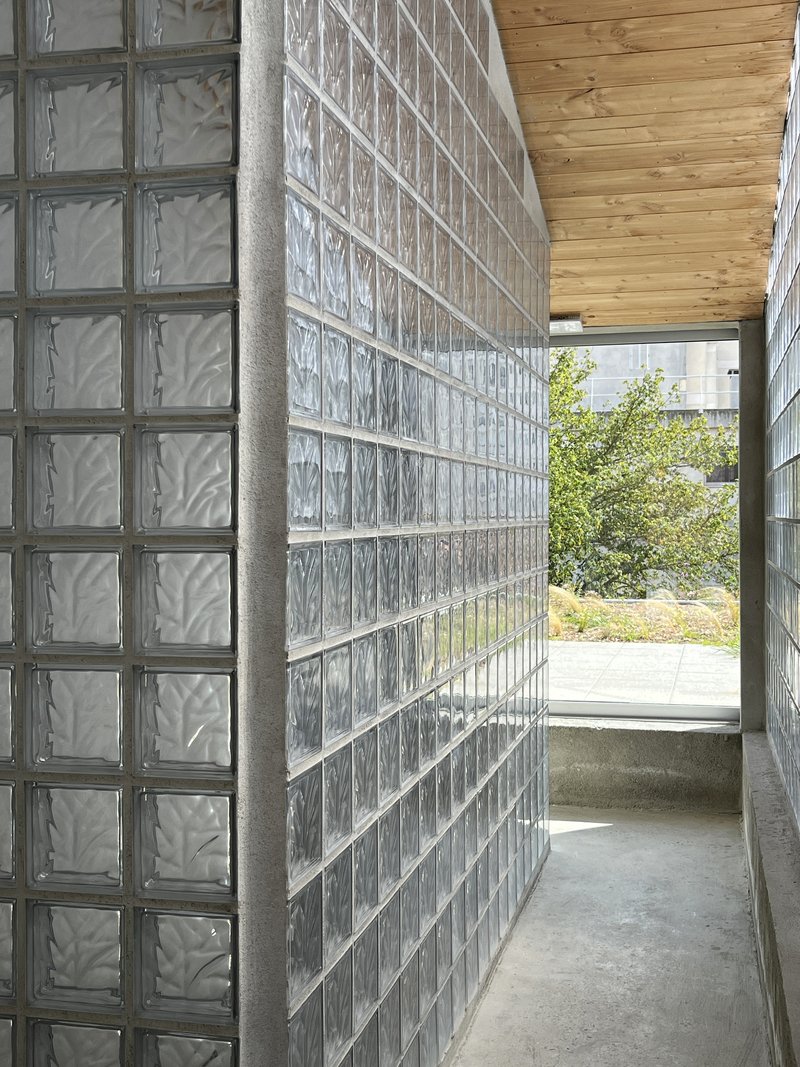 Corridor passage flanked by translucent glass block walls with timber ceiling opening to courtyard beyond