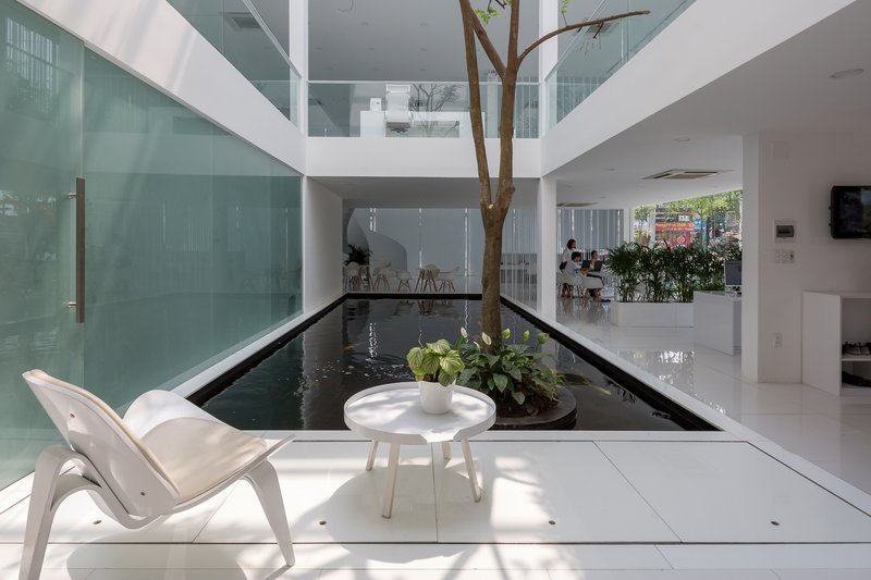 Ground floor interior water feature with planted tree and white lounge chair beside reflecting pool