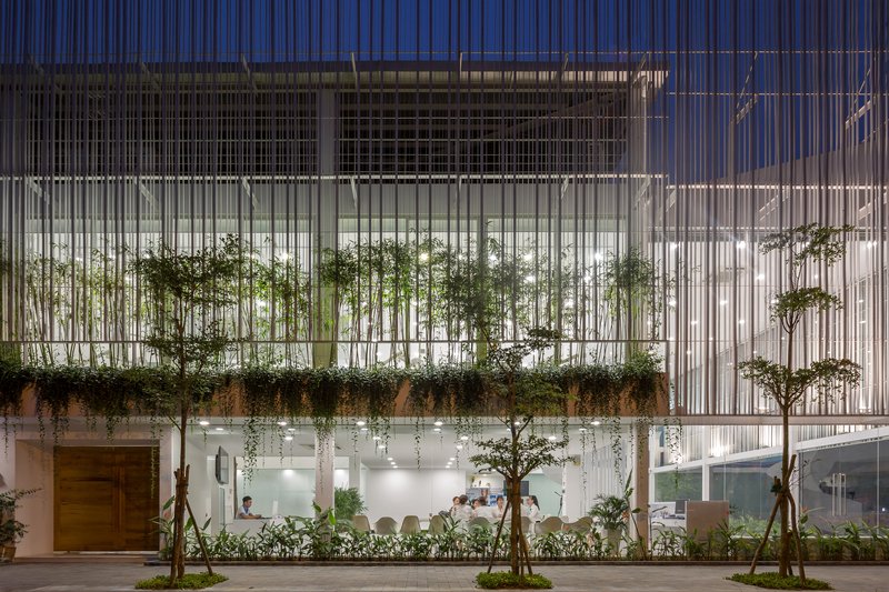 Street facade with vertical white slats screening planted terraces and interior spaces at dusk