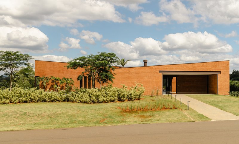 Red brick facade with vertical window slits and recessed timber garage door under white clouds