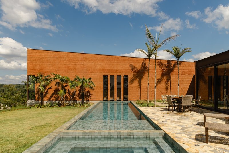 Lap pool with turquoise tile flanked by palms and stone terrace facing brick volume